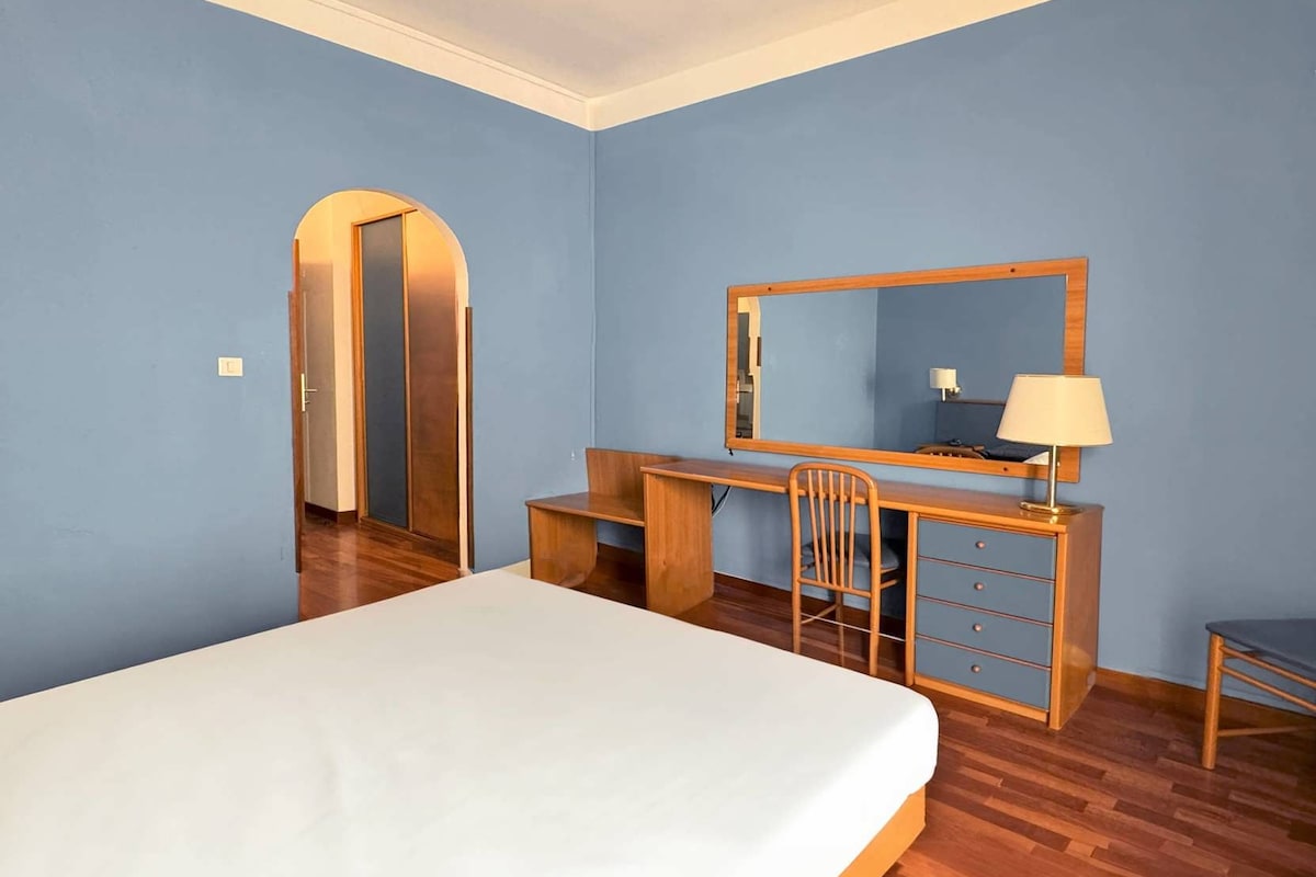 Habitación de hotel con cama, escritorio, silla, espejo y lámpara.