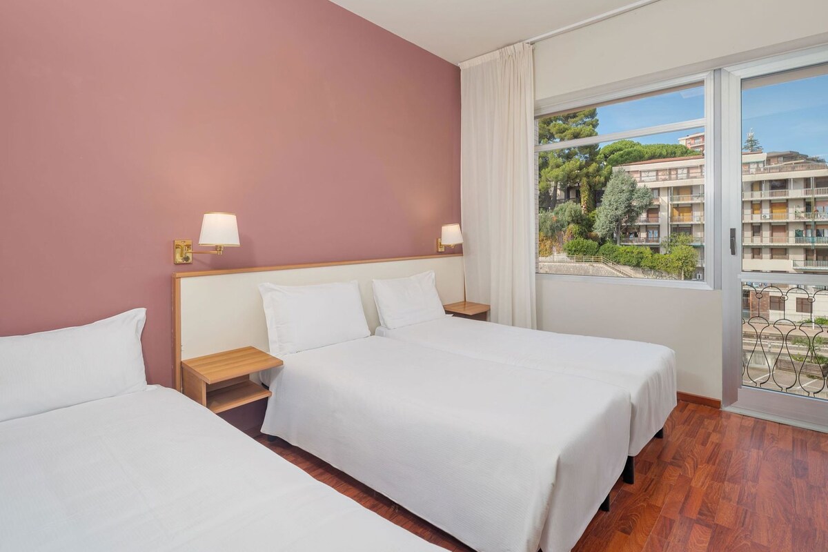 Habitación de hotel con dos camas, suelo de madera y vista a una zona residencial.