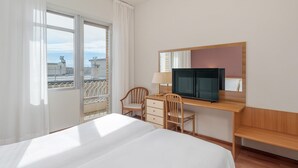 Habitación de hotel con cama, escritorio con televisor, una silla y ventana con vista a la ciudad.