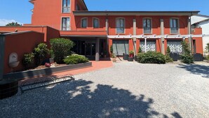 A red building with a covered entrance, multiple windows, and a gravel driveway. - Hotel Carignano (Lucca)