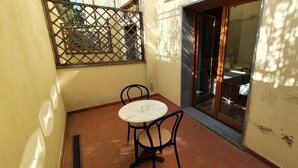 A small patio area with a round table and two chairs, a sliding glass door, and a metal gate. - Hotel Carignano (Lucca)