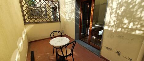 A small patio area with a round table and two chairs, a sliding glass door, and a metal gate.