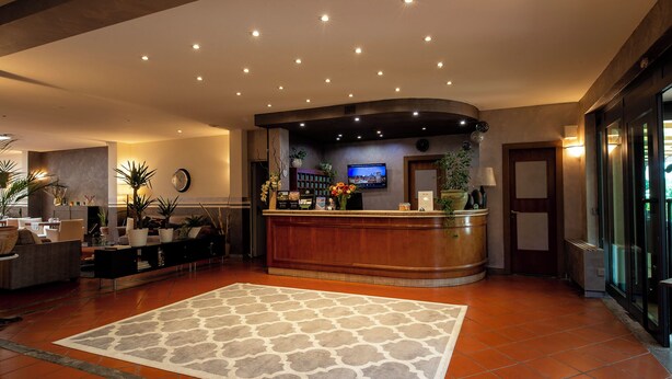 A hotel lobby with a reception desk, seating area, and a large patterned rug. - Hotel Carignano (Lucca)