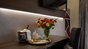 A modern hotel room with a wooden desk, a flat-screen TV mounted on the wall, a vase with flowers, and a chair. - Hotel Carignano (Lucca)