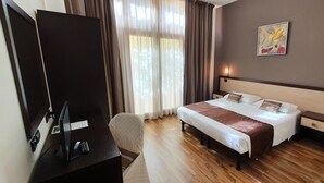 A hotel room with a bed, bedside tables, a desk with a computer and phone, a chair, and a window with curtains. - Hotel Carignano (Lucca)