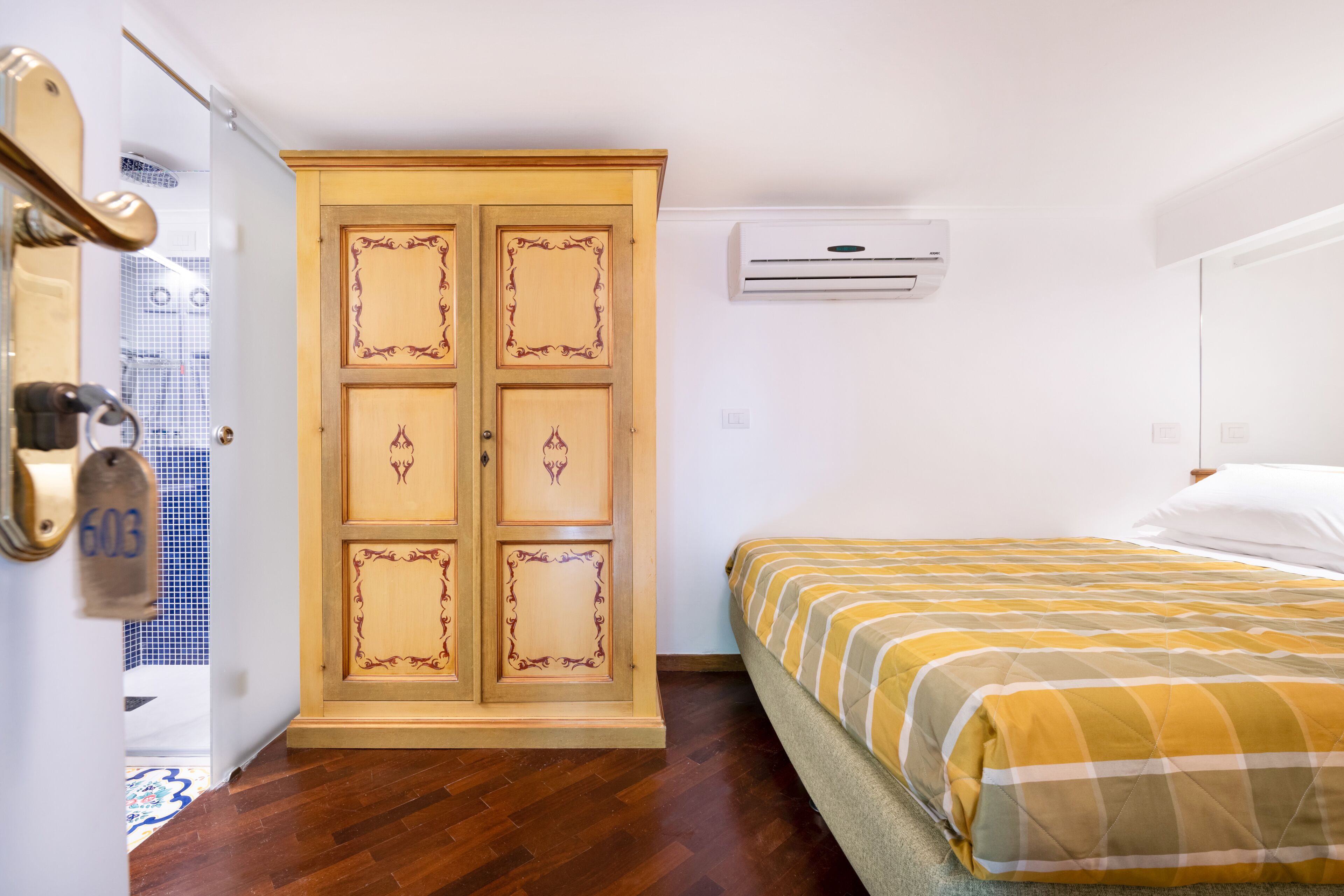 Una habitación de hotel con un armario de madera, una cama con colcha a rayas y un equipo de aire acondicionado en la pared.