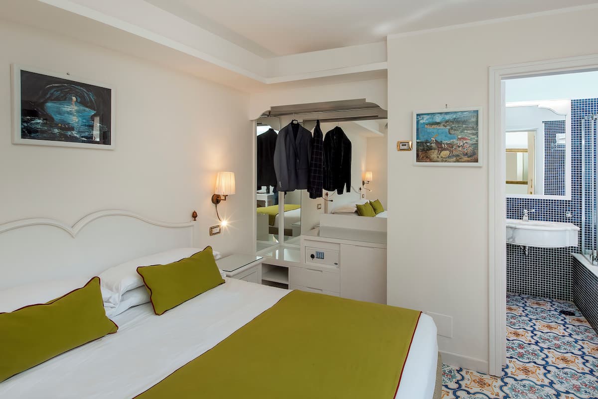 A hotel room with a bed, a dresser, a mirror, and a bathroom with a sink and tiled floor.