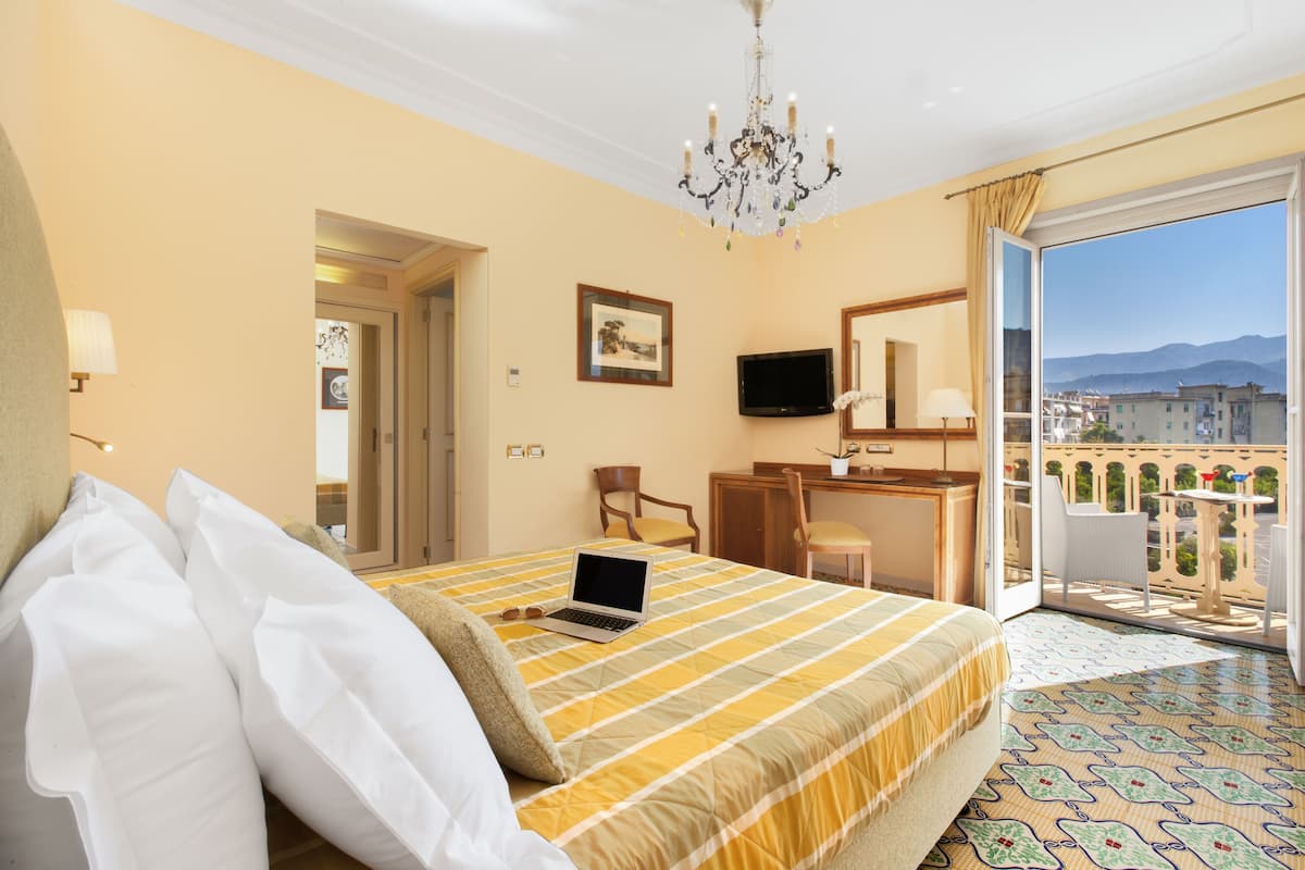 A hotel room with a bed, a desk, a laptop, a TV, and a balcony with a city view.