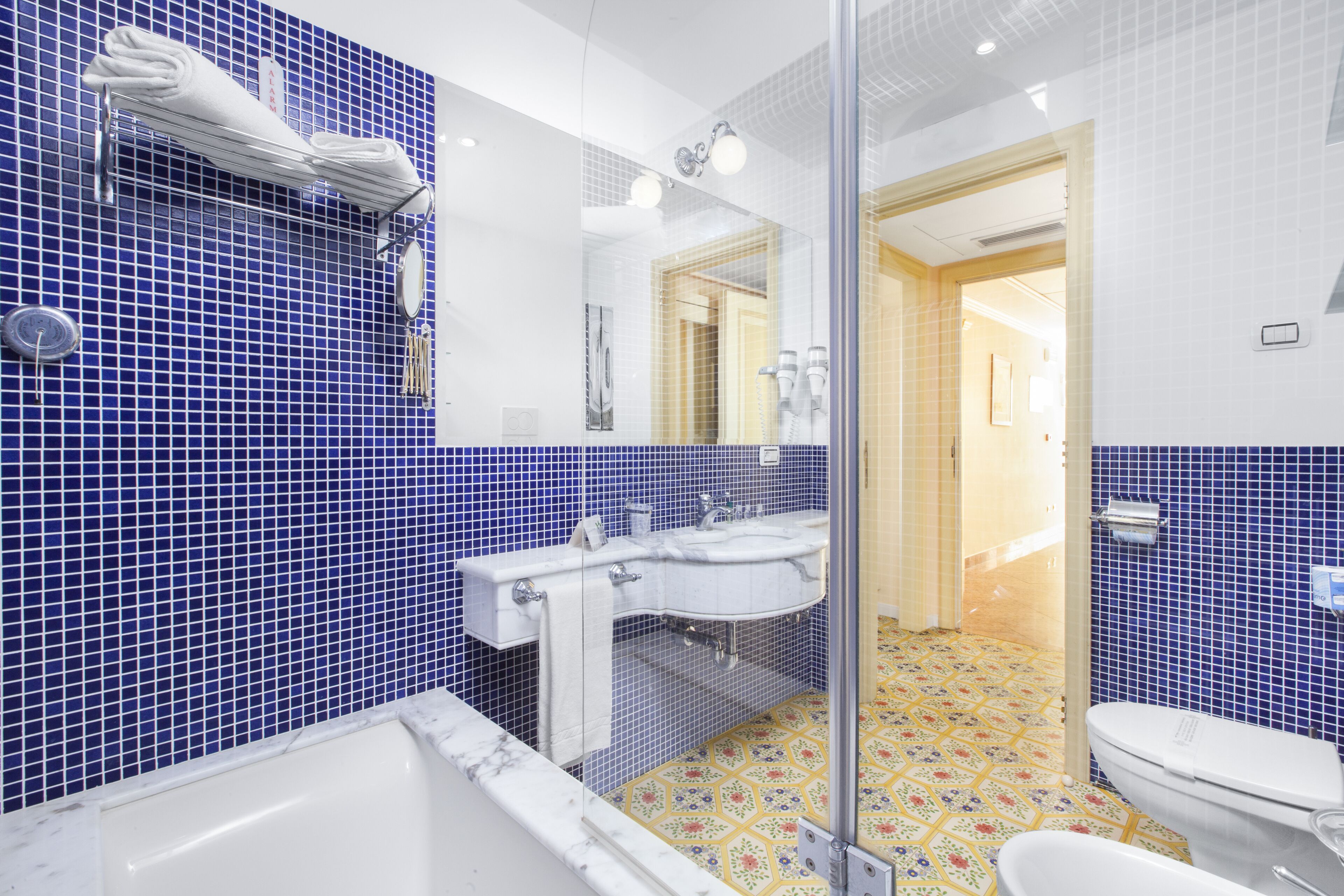 A bathroom with a blue tiled wall, a white sink, a mirror, and a toilet.