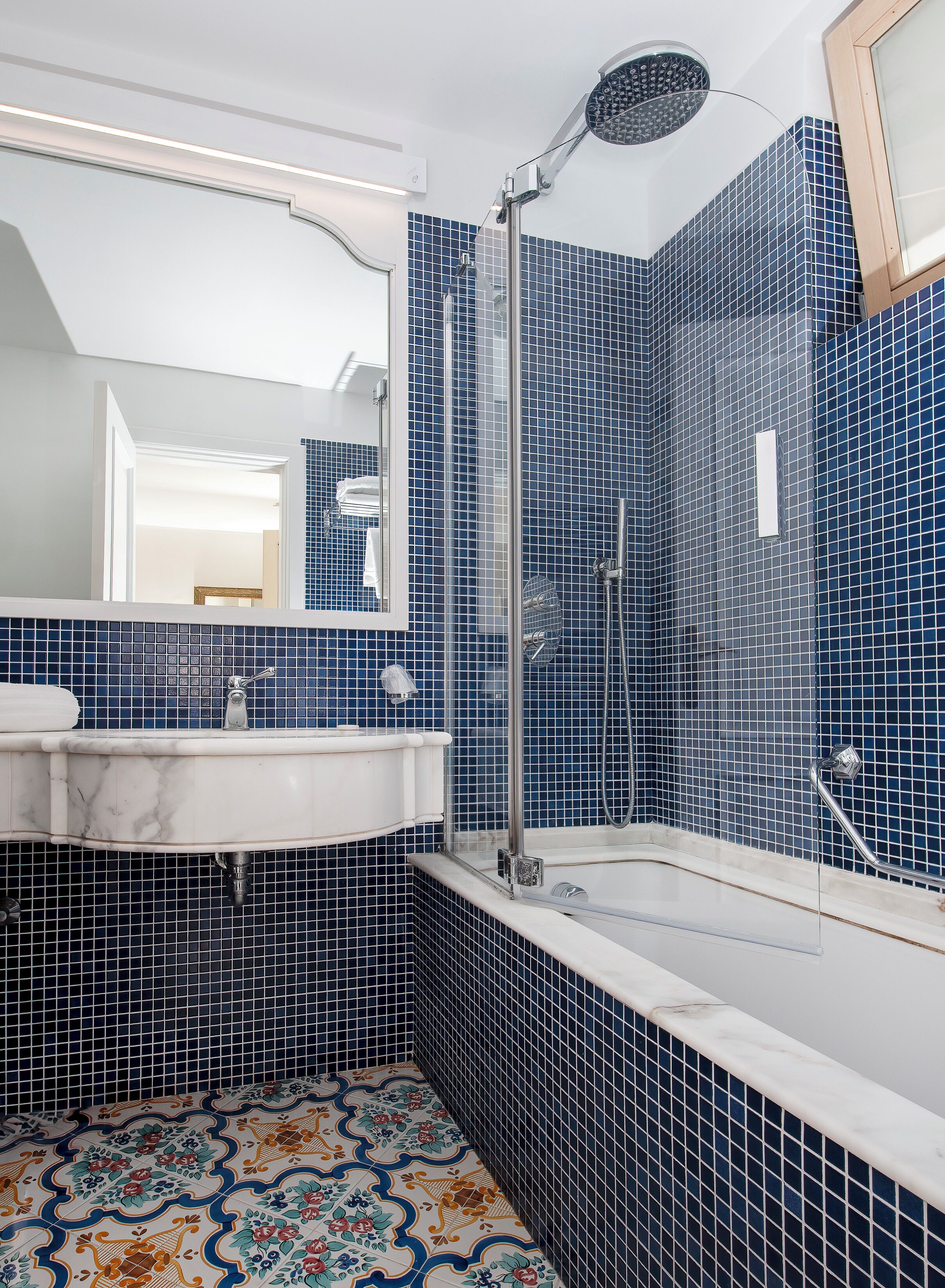 A bathroom with a white sink, a shower with a glass door, and blue-tiled walls.