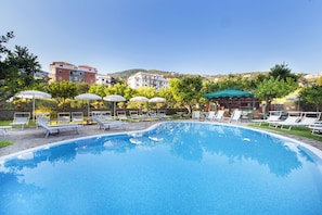 A swimming pool with lounge chairs and umbrellas, surrounded by trees and buildings in the background.