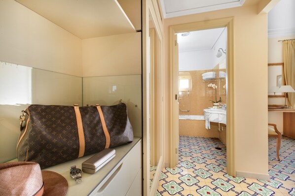 A hotel room with a bed, a suitcase, a watch, and a desk with a lamp.