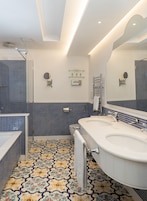Un baño con un lavamanos blanco, un espejo y una ducha. El piso tiene un estampado de azulejos coloridos.