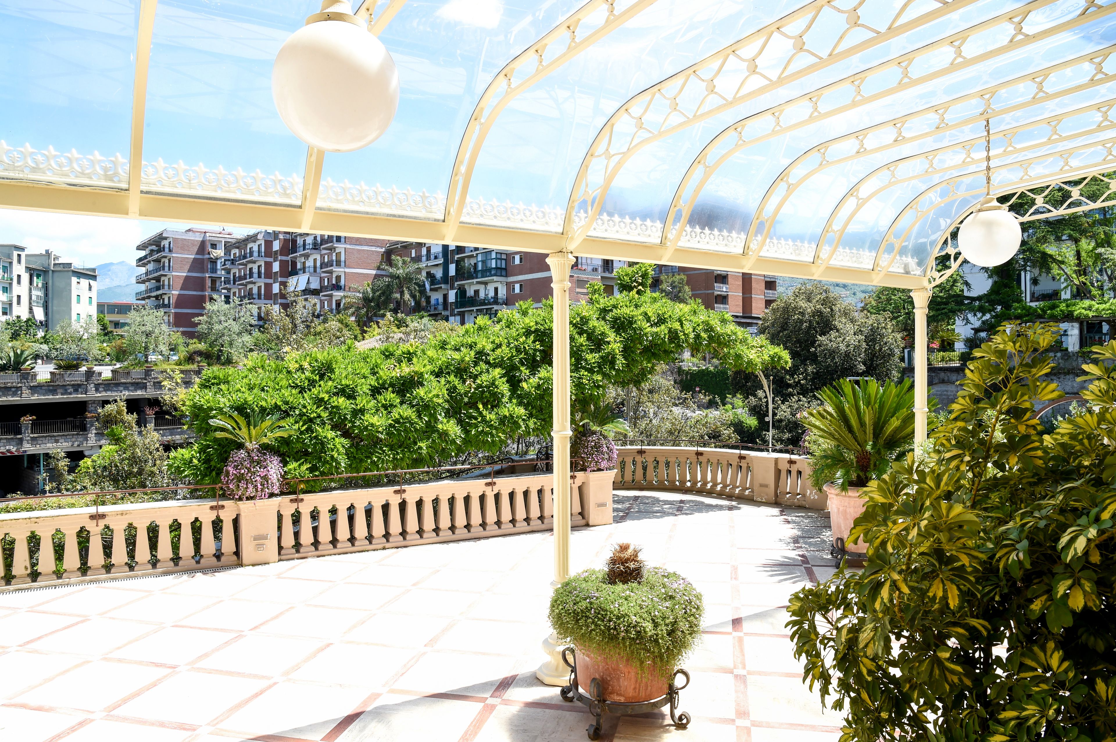 A covered outdoor area with a tiled floor, a metal railing, and potted plants.