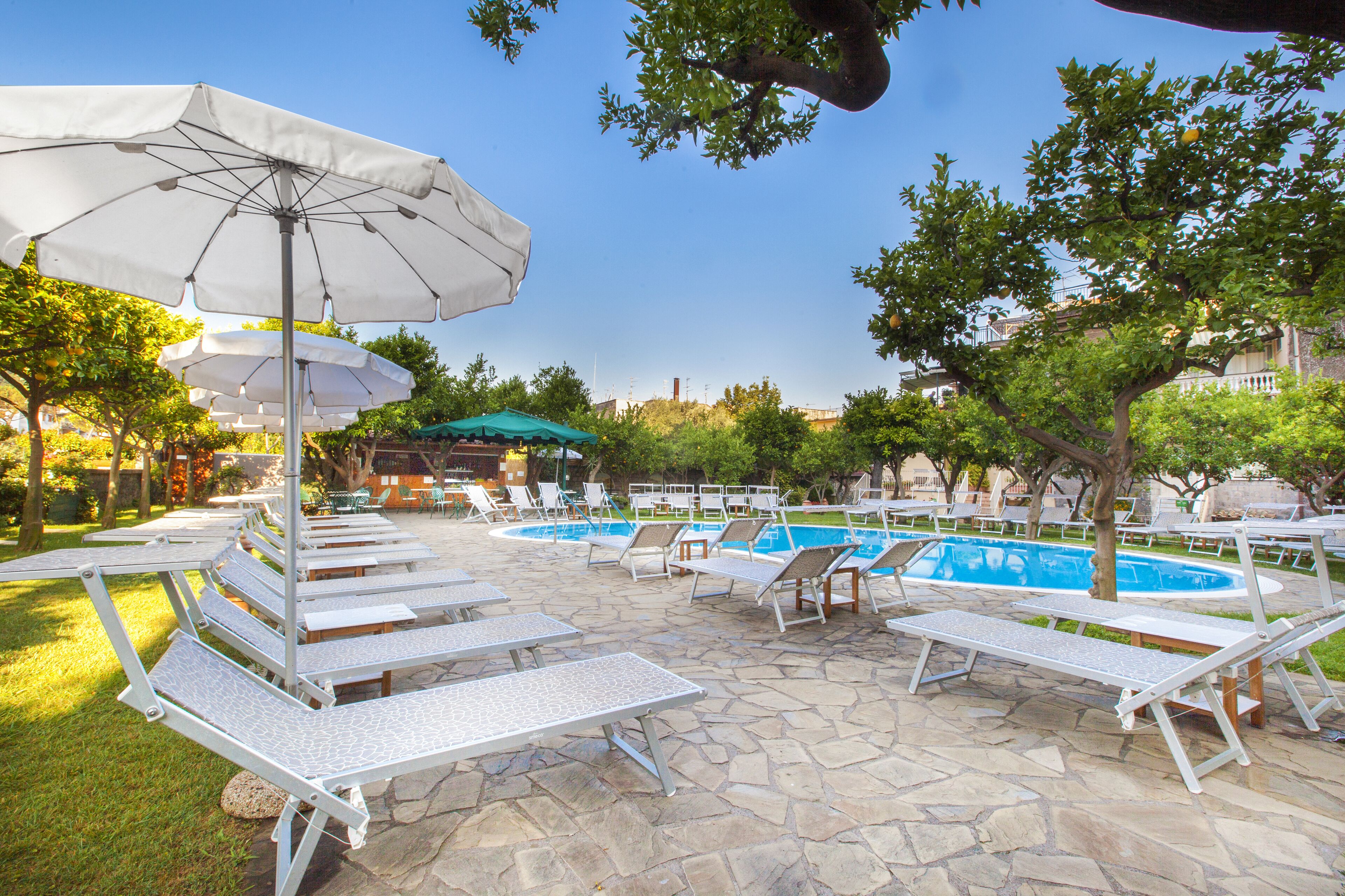 A poolside area with lounge chairs and umbrellas, a stone patio, and a swimming pool.