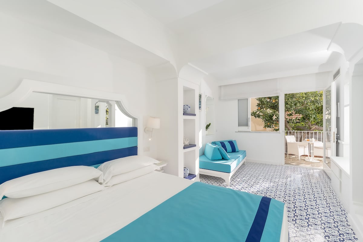 A hotel room with a large bed, a sofa, a balcony with a view, and a tiled floor.