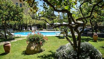Un espace piscine avec des chaises longues, un grand pot de fleurs et un arbre.