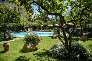 Un área de piscina con sillas de descanso, una maceta grande y un árbol.
