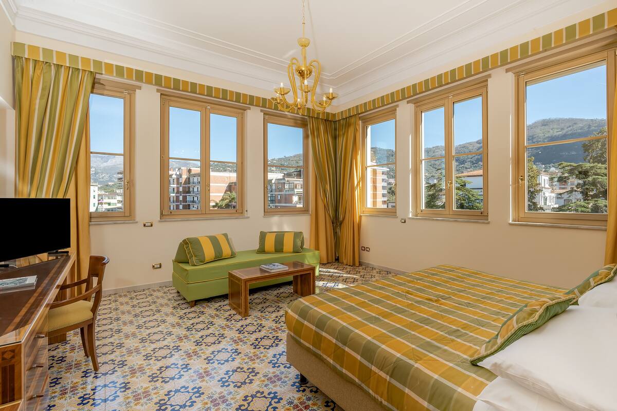 A hotel room with a large bed, a green sofa, a wooden desk, and a TV.