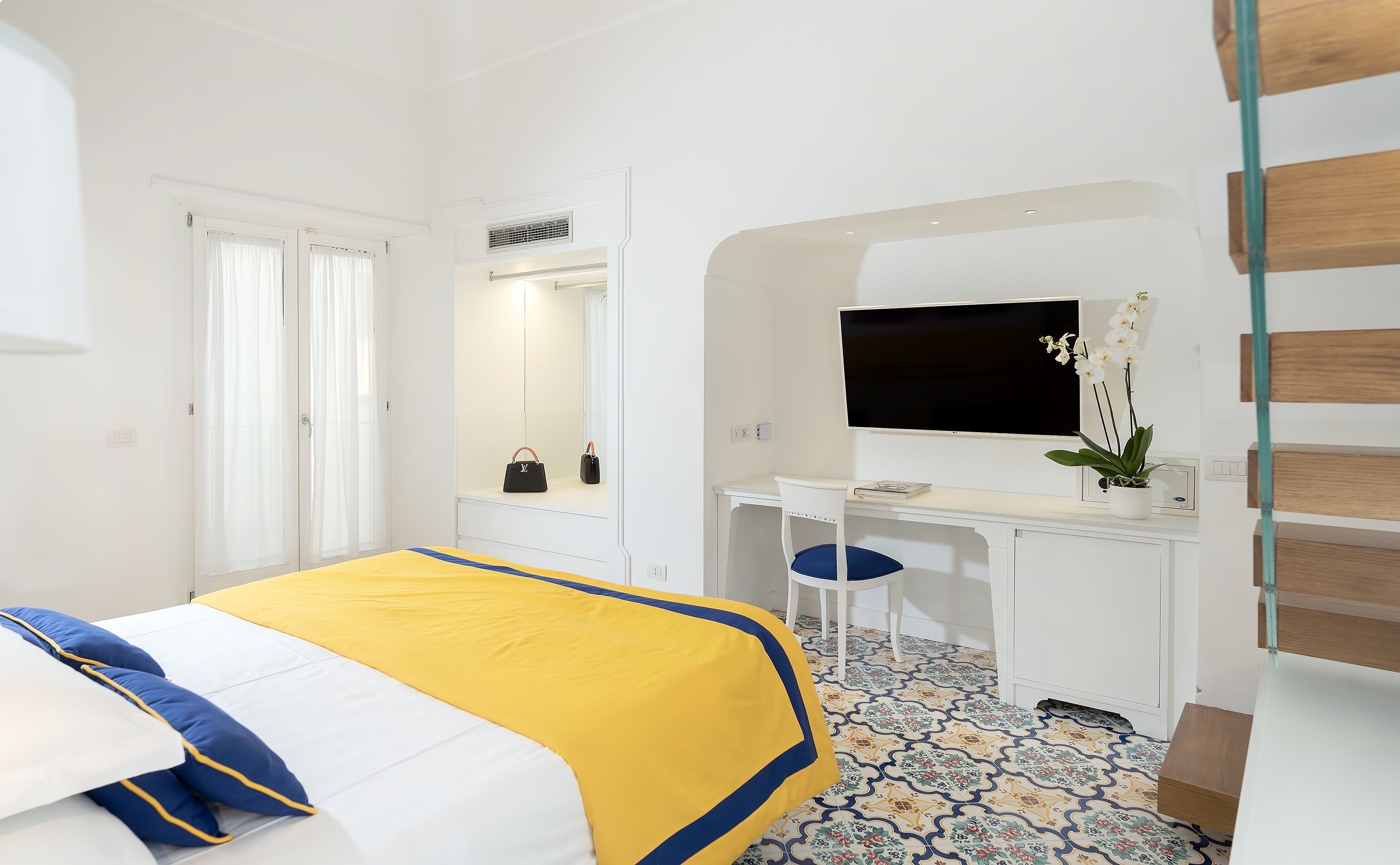 Quarto de hotel com uma cama, uma escrivaninha, uma cadeira, uma TV e um vaso de plantas.