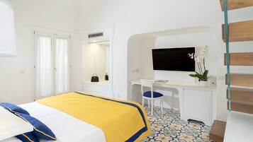 Quarto de hotel com uma cama, uma escrivaninha, uma cadeira, uma TV e um vaso de plantas.