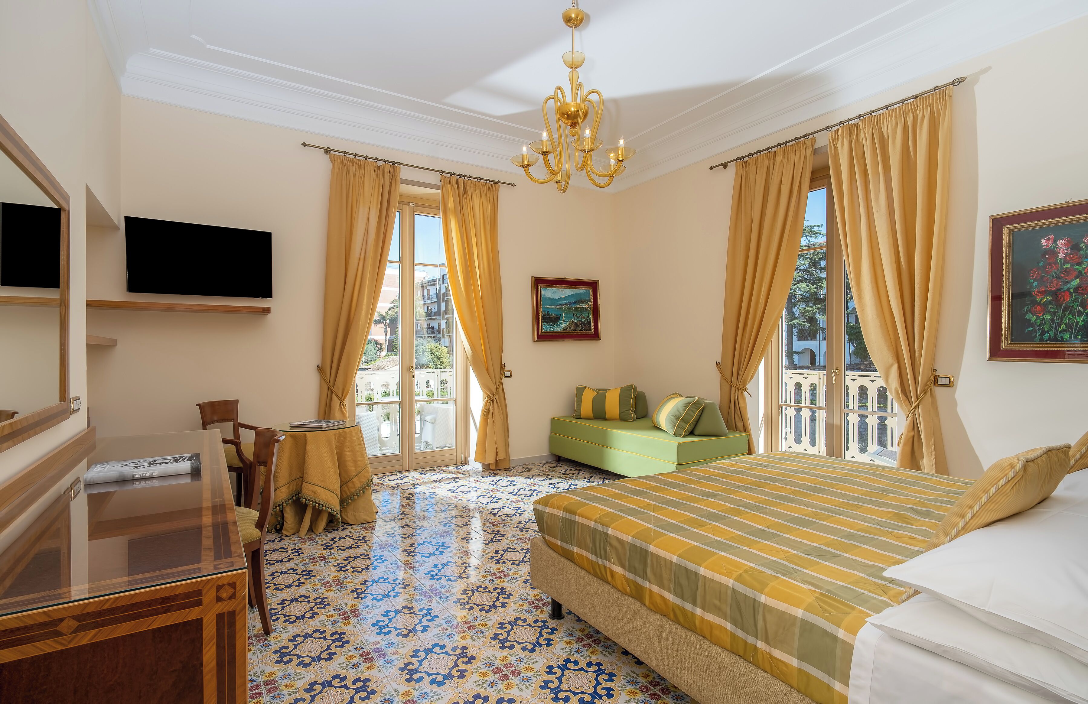 A hotel room with a large bed, a TV mounted on the wall, a dining table, and a view of the city through the windows.