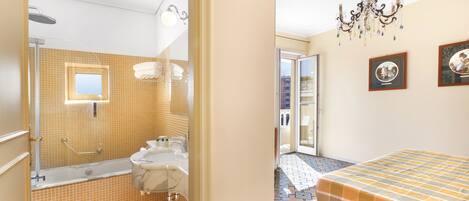 Un baño con bañera, ducha y lavamanos, y un dormitorio con cama y candelabro.