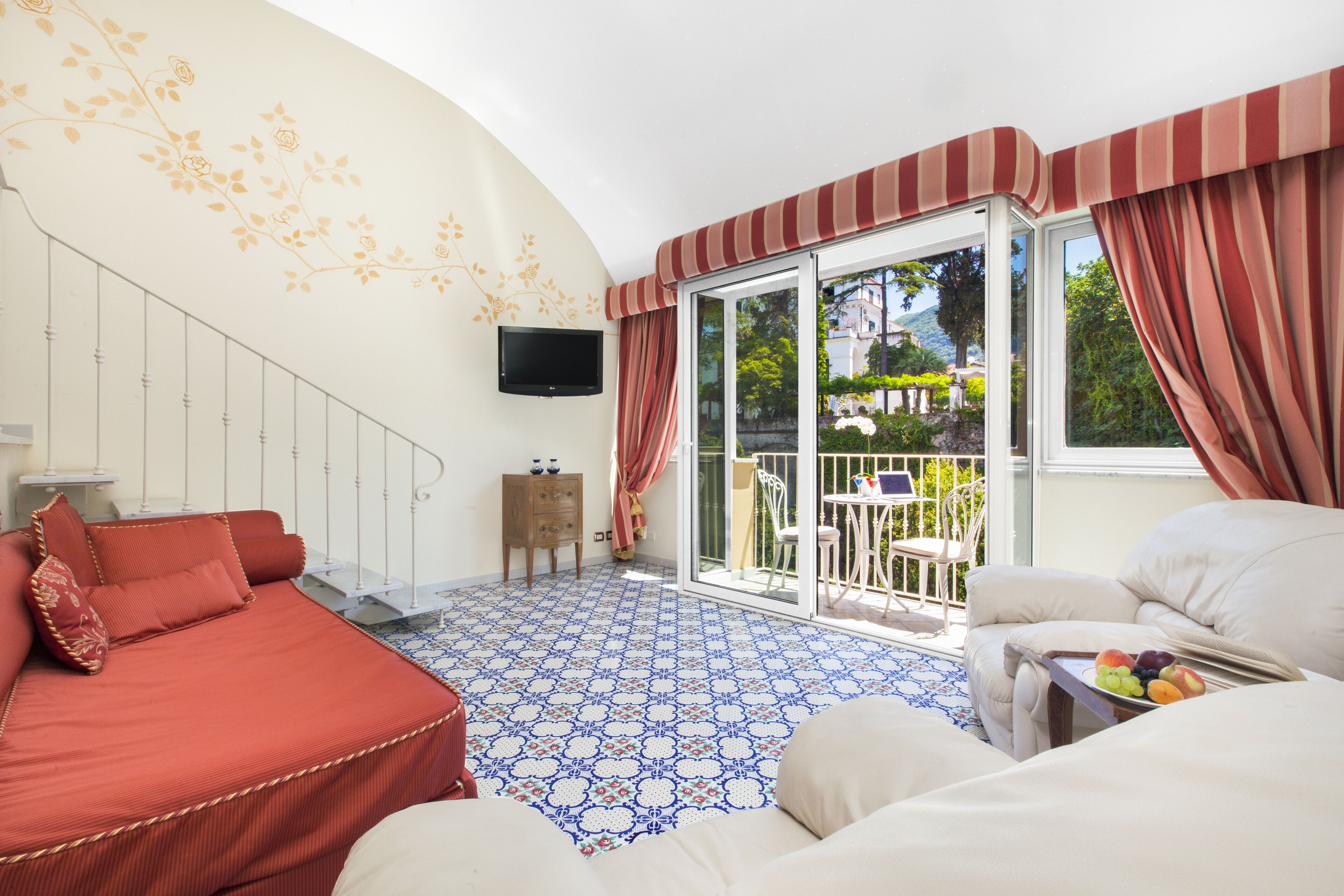 Ein Zimmer mit Bett, einer Couch, einem Fernseher und einem Balkon mit Tisch und Stühlen.