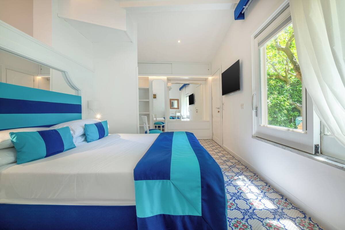 A bedroom with a bed, a TV, a window, and a mirror.