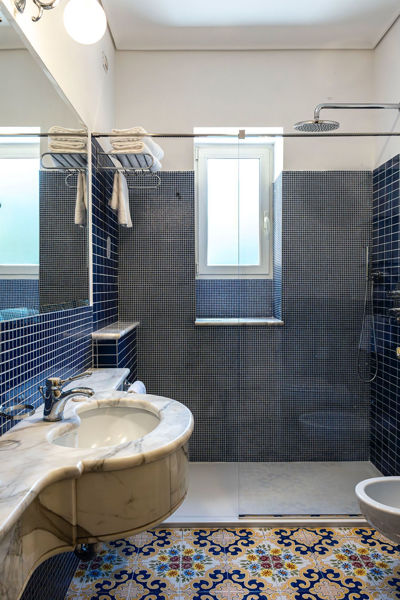 A bathroom with a marble sink, a shower, and a window.