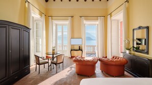 Une chambre d’hôtel avec un grand lit, deux fauteuils, une table à manger avec des chaises, un téléviseur et une vue sur la mer.