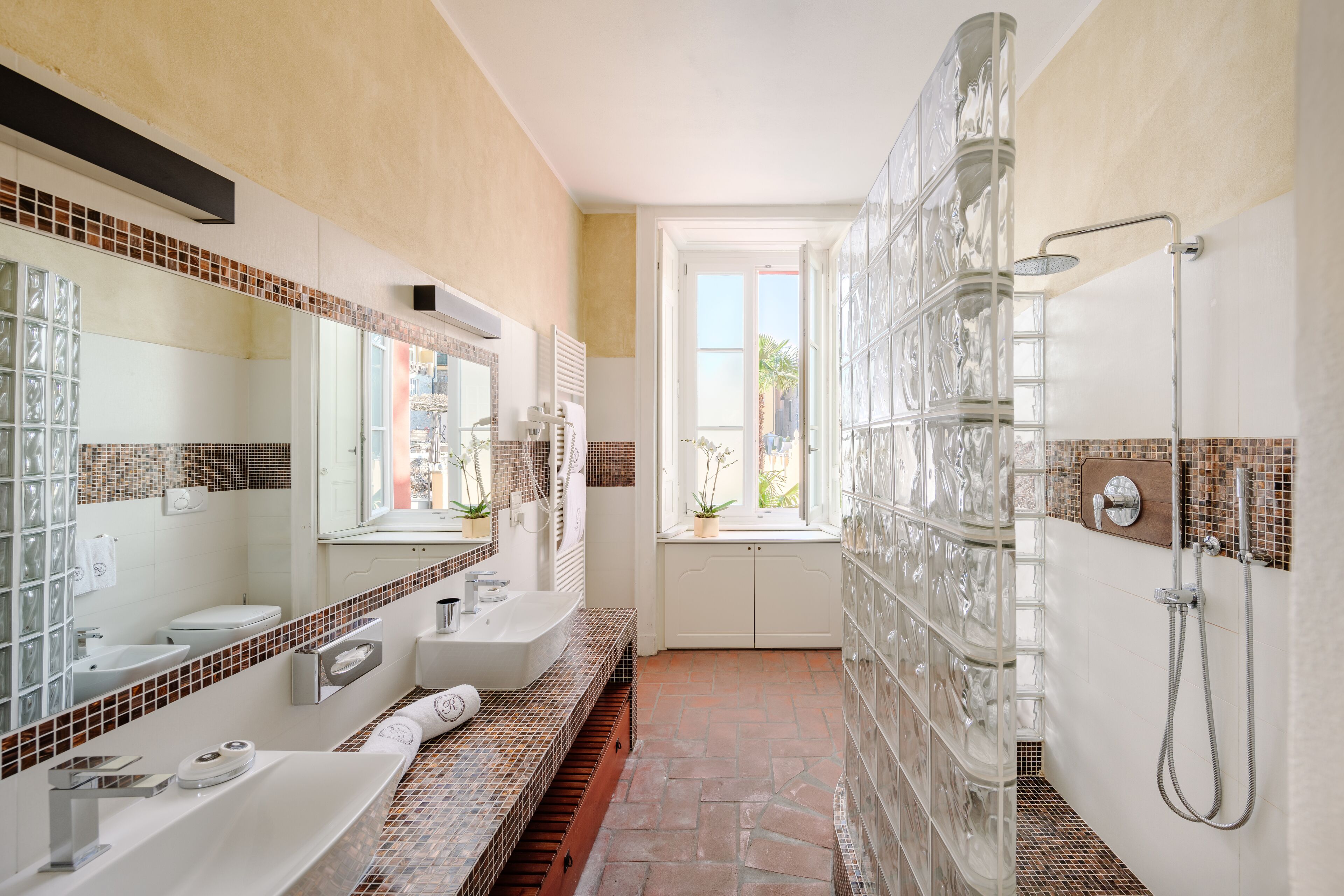 A modern bathroom with a glass shower enclosure, a large mirror, and a window providing a view of the outdoors.