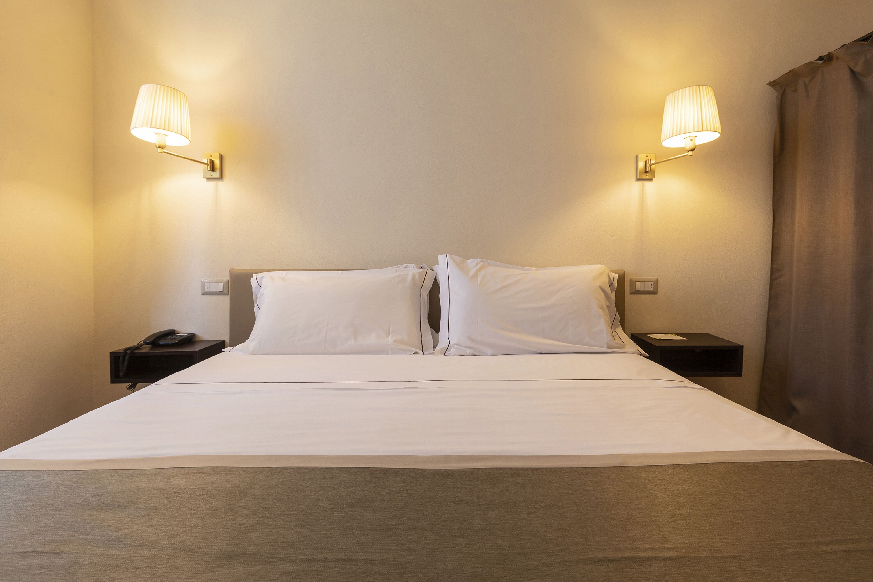 A hotel room with a large bed, two bedside tables, and two wall-mounted lamps.