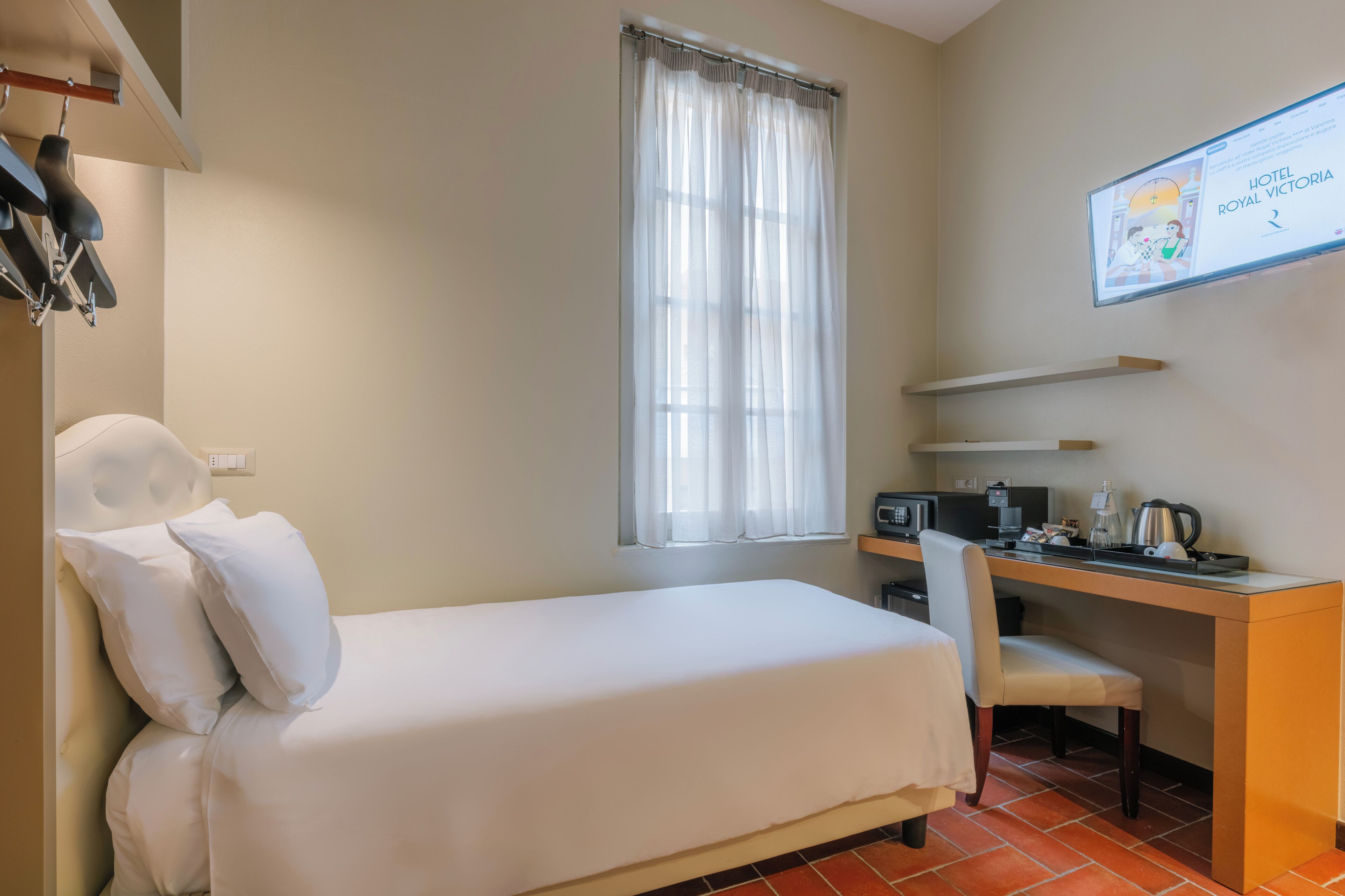 A hotel room with a bed, a desk with a chair, a computer, and a coffee maker.
