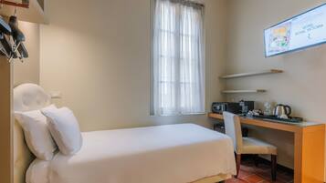 A hotel room with a bed, a desk with a chair, a computer, and a coffee maker.
