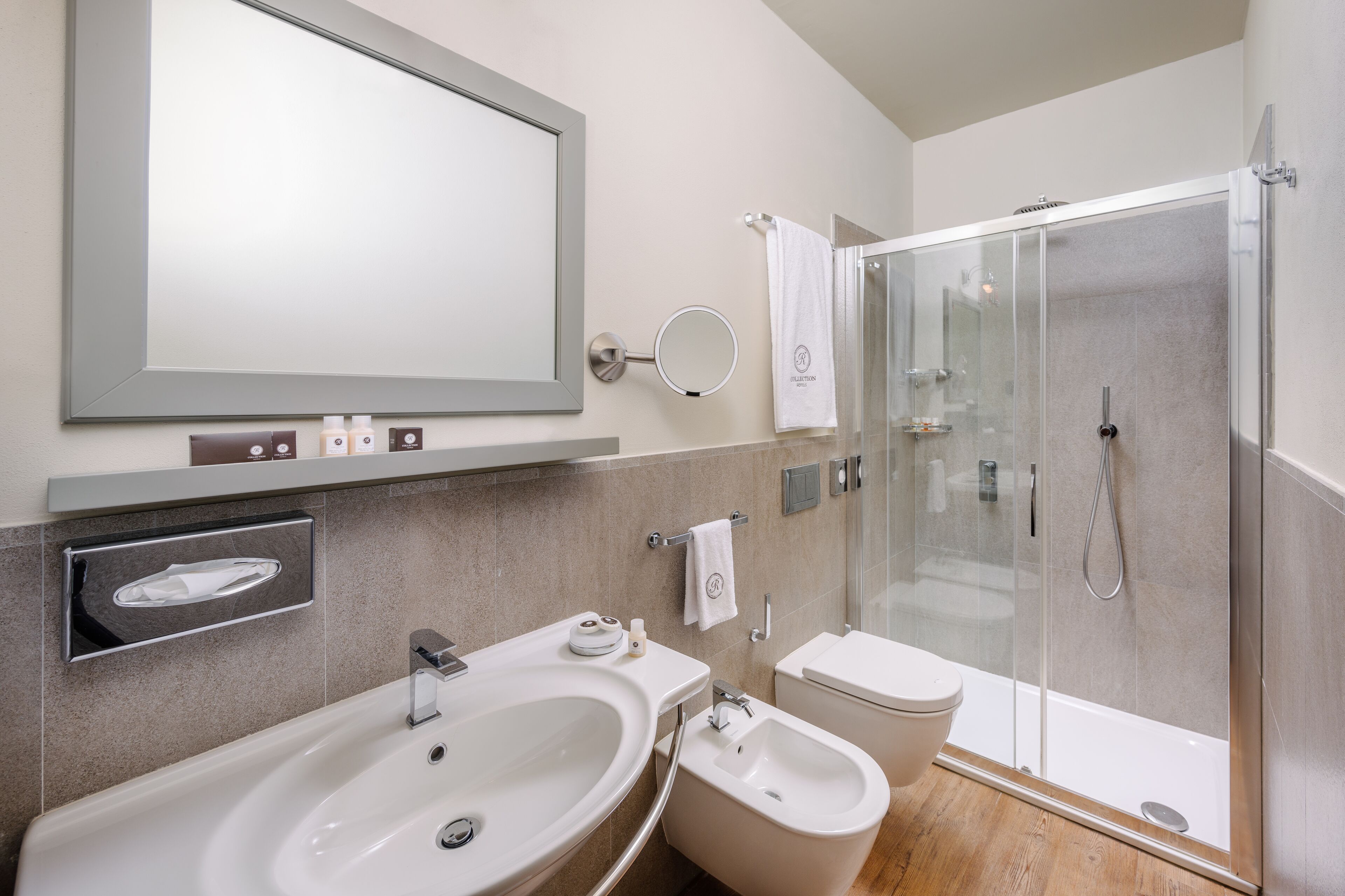 Un baño moderno con un espejo grande, dos lavamanos, un bidé y una ducha con mampara de vidrio.