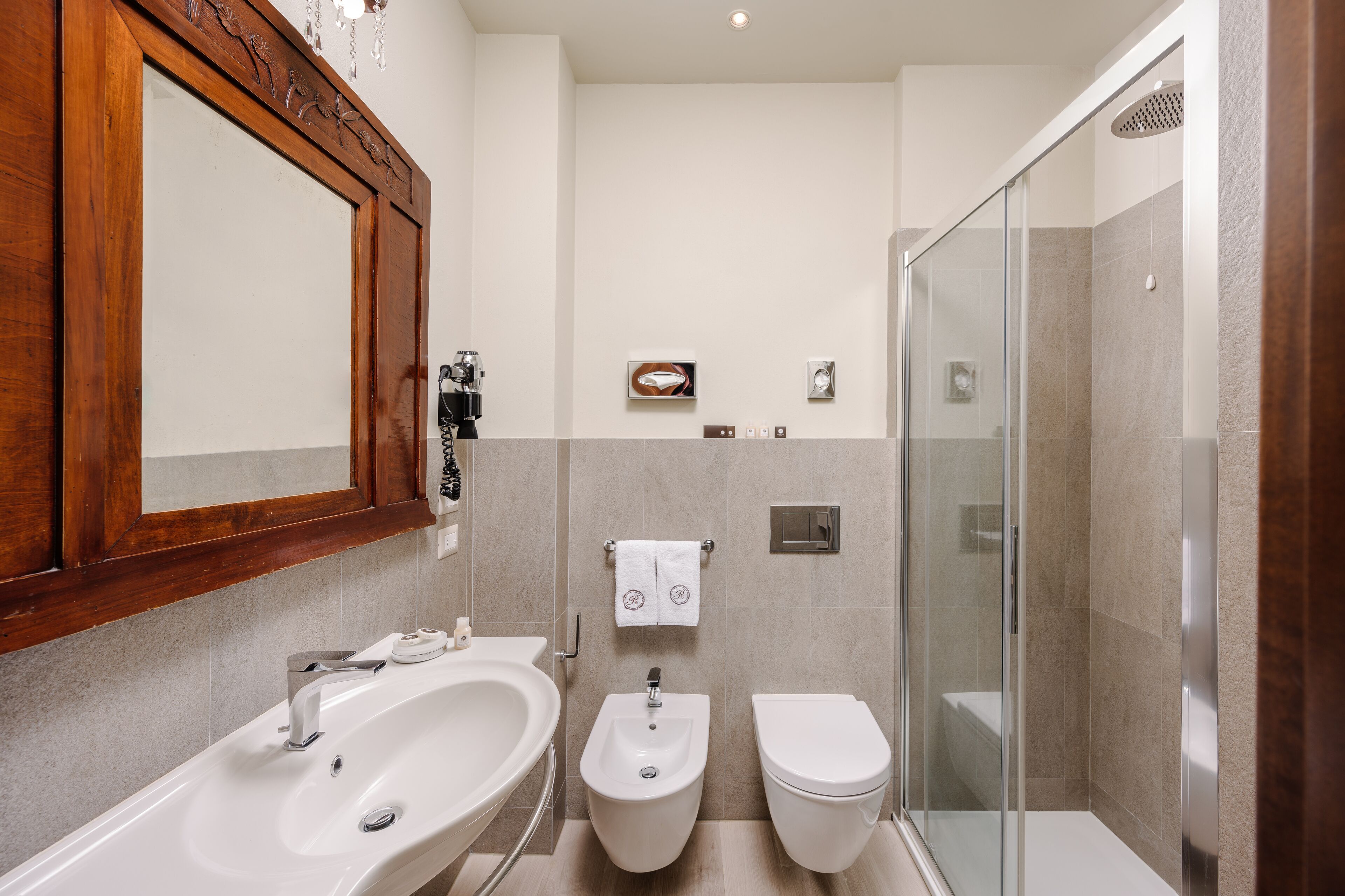 Une salle de bain avec un meuble-lavabo en bois, un bidet, des toilettes et une douche à parois de verre.
