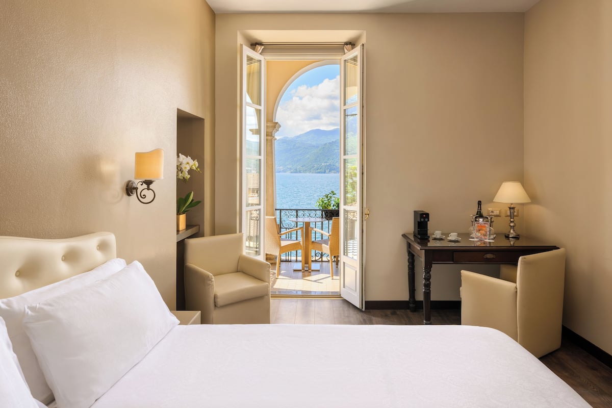 A hotel room with a bed, a desk, a chair, and a view of a lake through an open door.