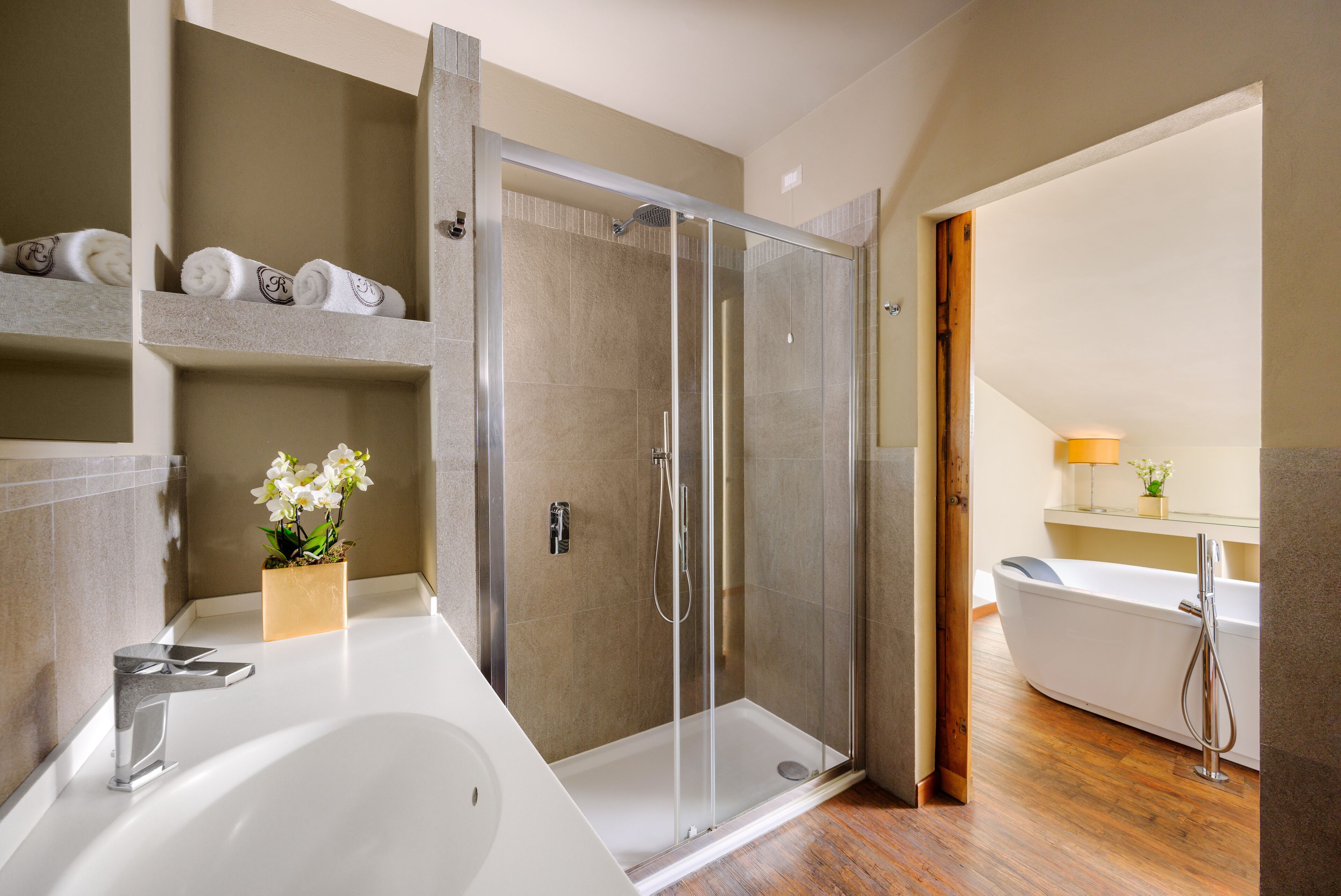 Un baño moderno con ducha de vidrio, una bañera independiente y un tocador con lavamanos y barra para toallas.