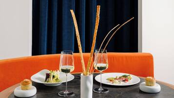 A dining table with two plates of food, two glasses of wine, and a pastry on a modern orange couch.