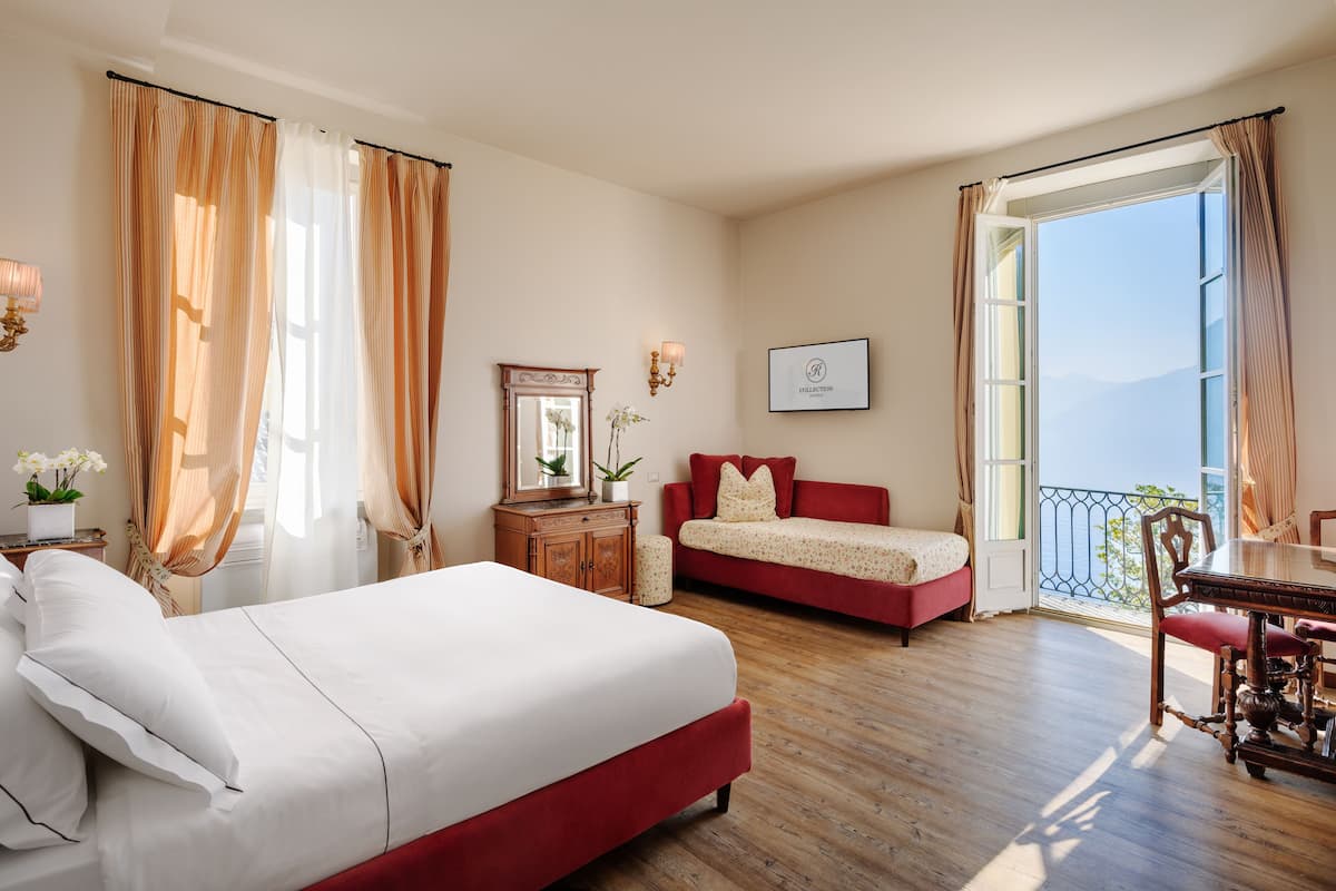 A hotel room with a bed, a sofa, a dining table, and a view of the outdoors.