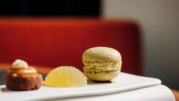 Ein weißer Teller mit drei Desserts: einem Macaron, einem kleinen Törtchen und einem Zitronenschnitzel.