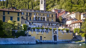 Un hôtel historique doté d’un clocher, situé au bord de l’eau, avec un mur de pierre et une végétation luxuriante.