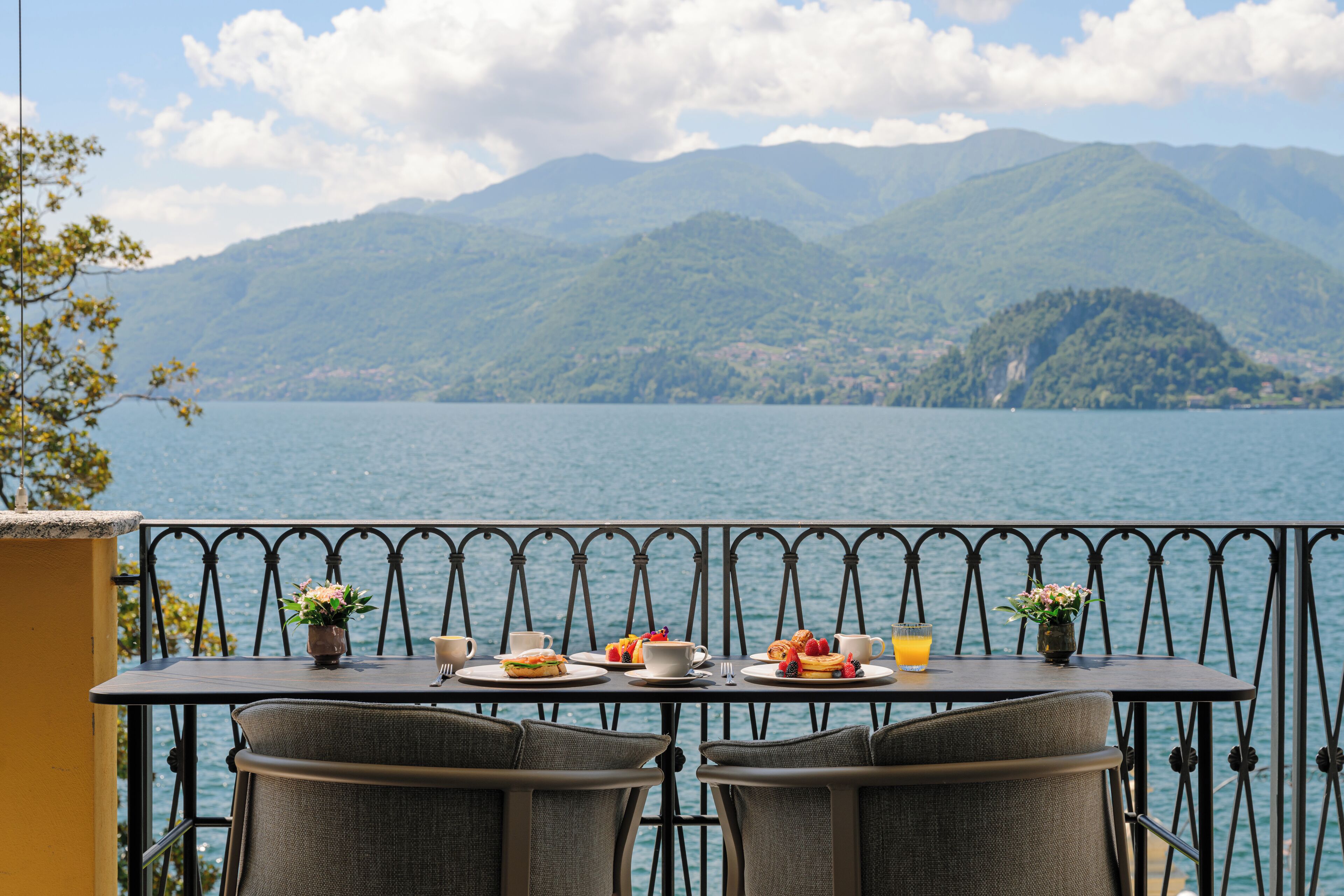 A table with plates of food and drinks, overlooking a lake with mountains in the background.