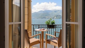 Un balcon ouvert, agrémenté de fauteuils et d’une table en osier, offrant une vue sur un lac et des montagnes.