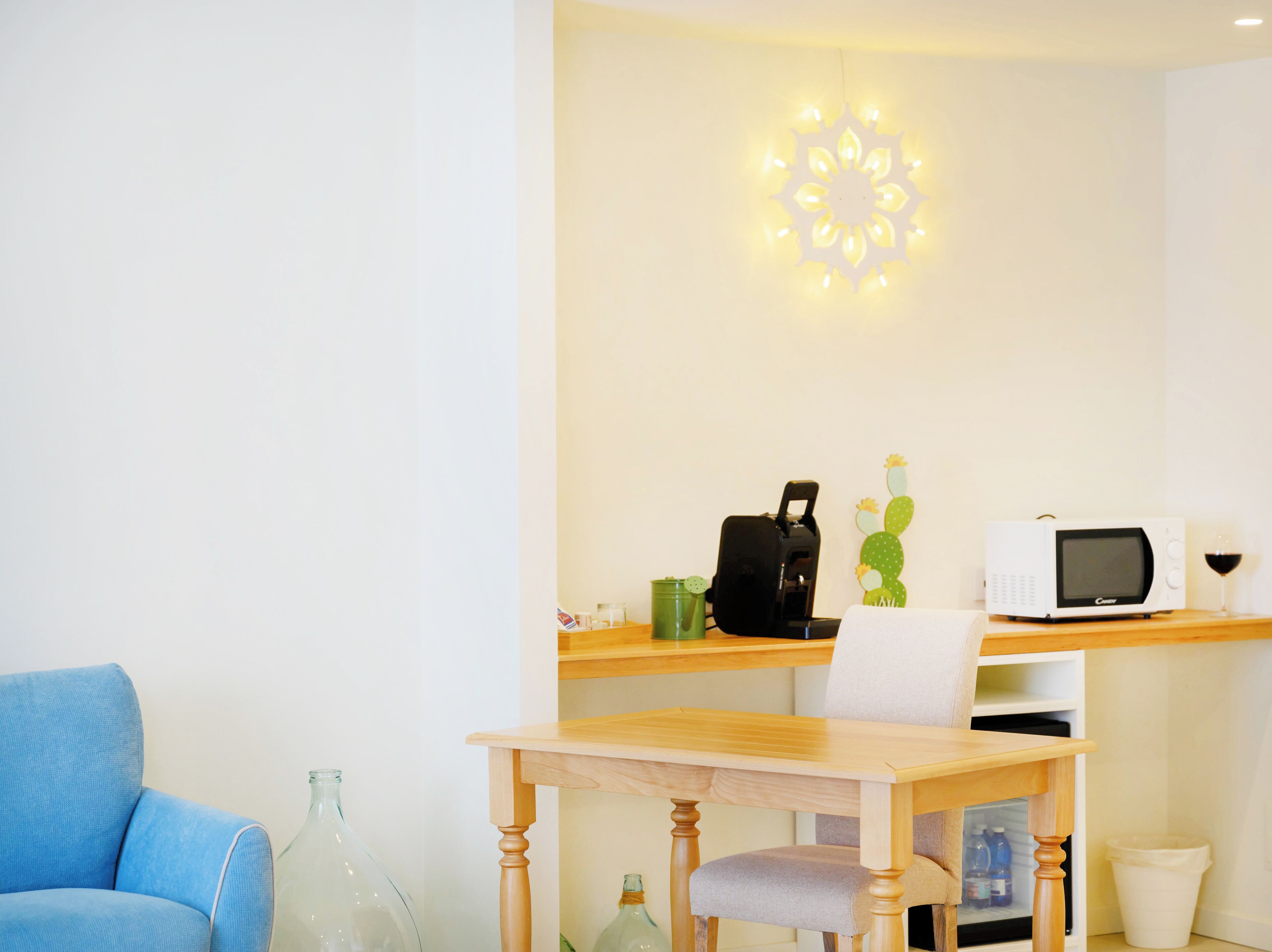 A compact living space with a wooden table, a blue chair, a microwave, a coffee maker, and a cactus decoration.