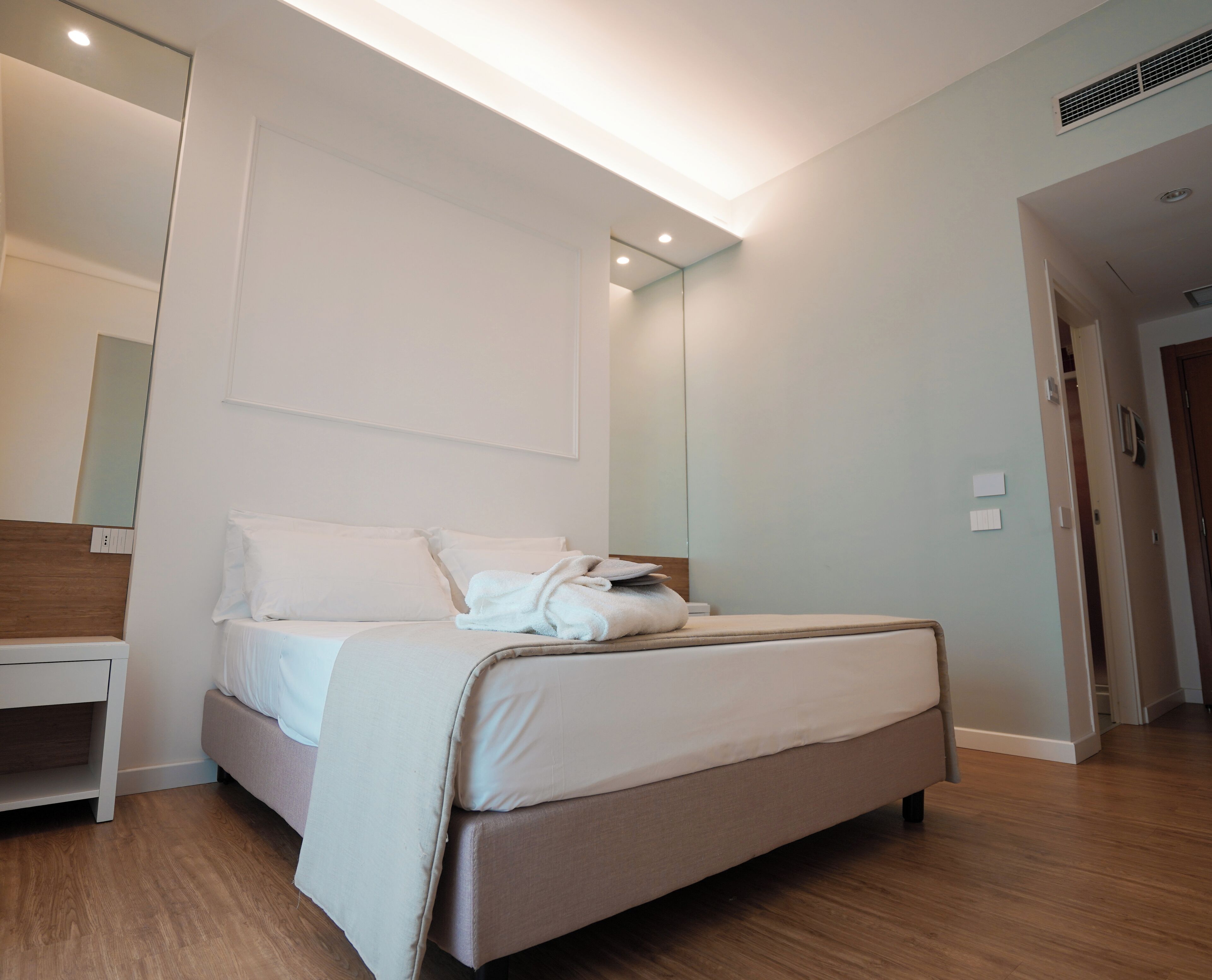 A modern bedroom with a bed, bedside table, and a large mirror.