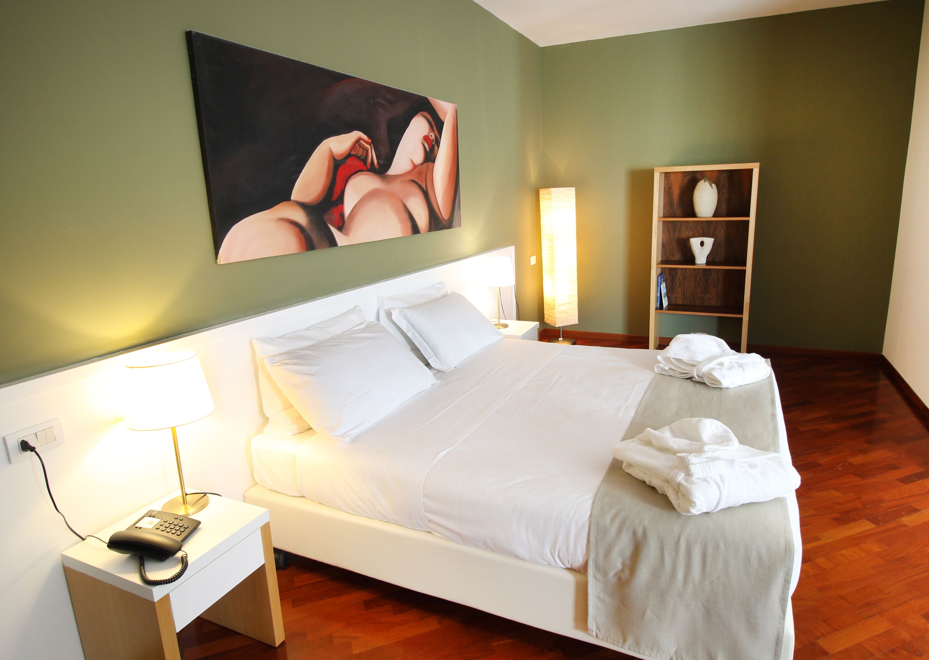 Une chambre d’hôtel avec un lit, une lampe de chevet, un téléphone, un tableau au mur et une étagère avec des serviettes.