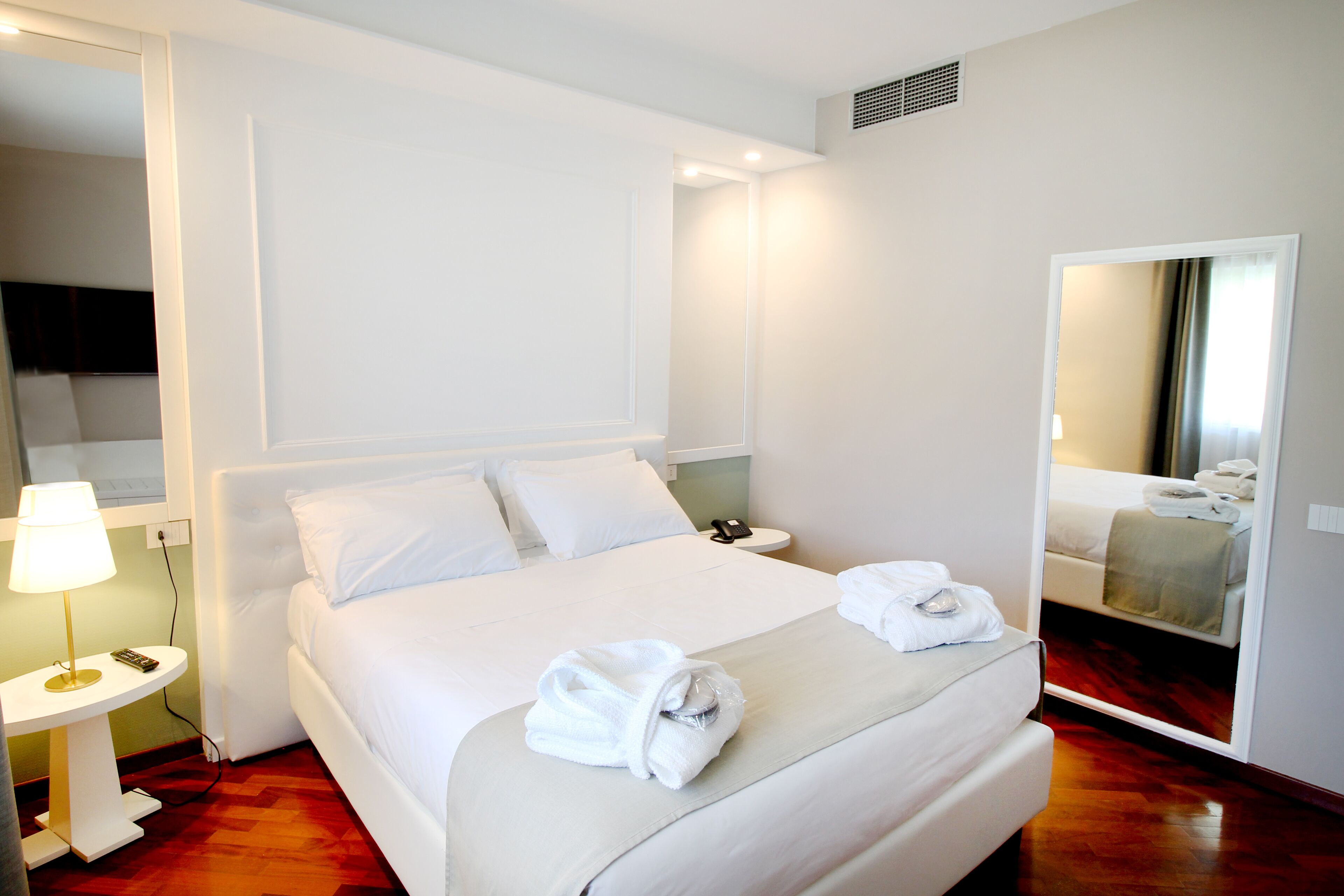 A hotel room with a large bed, a bedside table with a lamp, a mirror, and a bathroom visible through an open door.