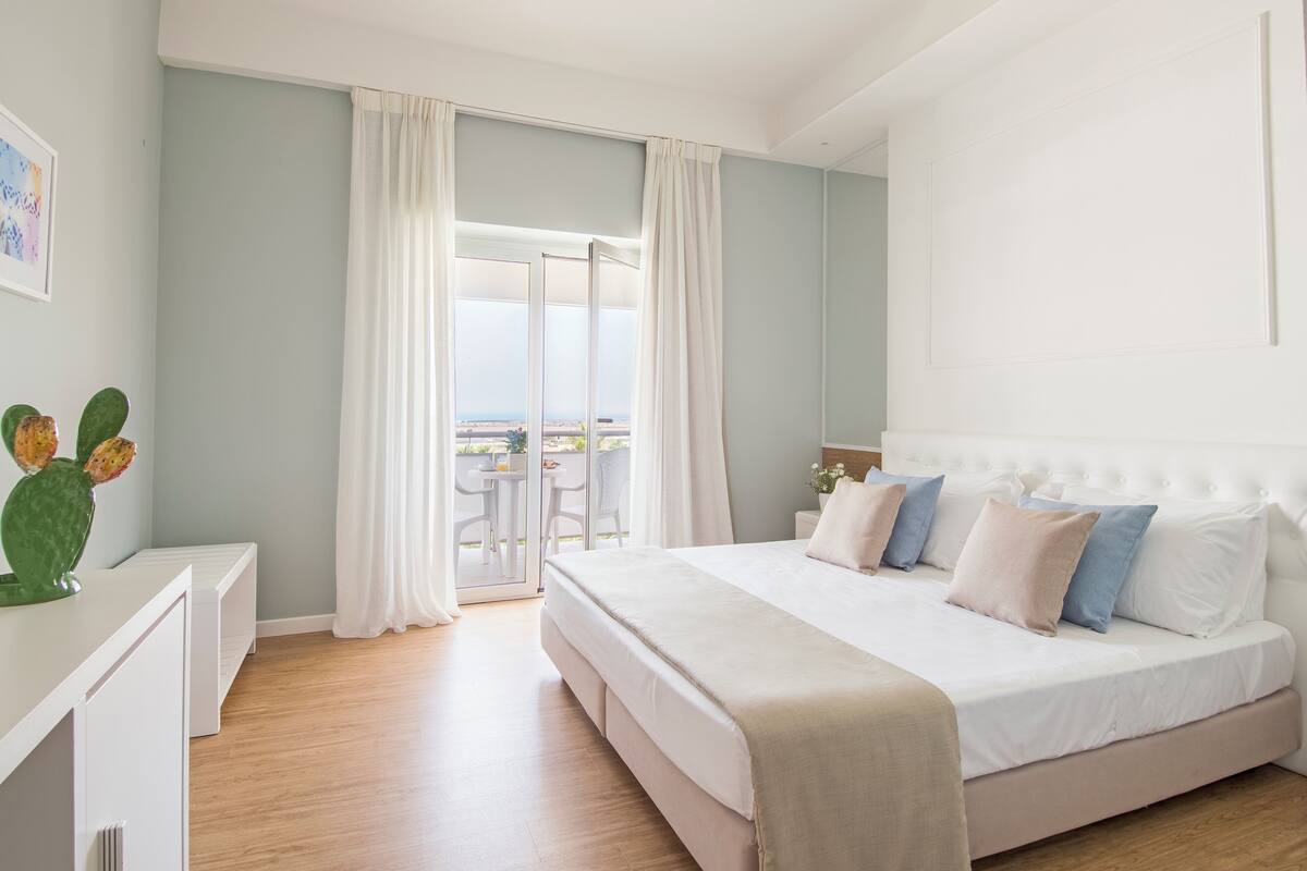 Un dormitorio con una cama grande, una mesita de noche, una silla y vistas al exterior.
